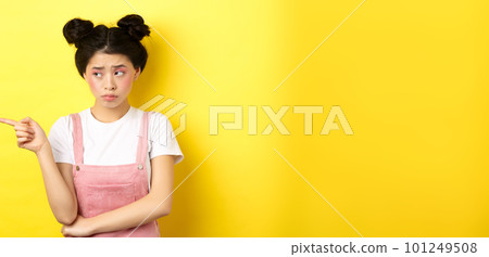 Upset frowning teenage girl sulking, pointing fingers left with jealous unfair face, standing disappointed on yellow background 101249508