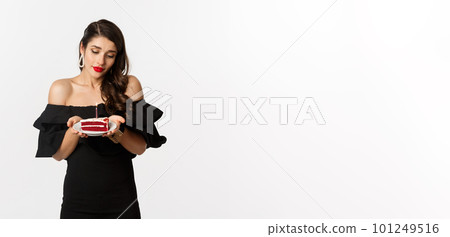 Party and celebration. Cute young woman with red lips, wearing black dress, holding birthday cake with candle and looking dreamy, making wish, white background 101249516