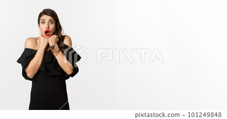Portrait of glamour woman looking scared and shocked at camera, staring at something with fear, standing in black dress against white background Portrait of glamour woman looking scared and shocked at camera, staring at something with fear, standing in black dress against white background 101249848