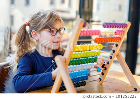 Little preschool girl playing with educational wooden rainbow toy counter abacus. Healthy happy child with glasses learning to count and colors, indoors on sunny day. 101253222