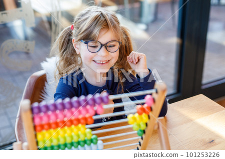 Little preschool girl playing with educational wooden rainbow toy counter abacus. Healthy happy child with glasses learning to count and colors, indoors on sunny day. Little preschool girl playing with educational wooden rainbow toy counter abacus. Healthy happy child with glasses learning to count and colors, indoors on sunny day. 101253226