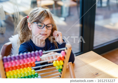 Little preschool girl playing with educational wooden rainbow toy counter abacus. Healthy happy child with glasses learning to count and colors, indoors on sunny day. Little preschool girl playing with educational wooden rainbow toy counter abacus. Healthy happy child with glasses learning to count and colors, indoors on sunny day. 101253227
