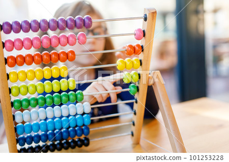 Little preschool girl playing with educational wooden rainbow toy counter abacus. Healthy happy child with glasses learning to count and colors, indoors on sunny day. Little preschool girl playing with educational wooden rainbow toy counter abacus. Healthy happy child with glasses learning to count and colors, indoors on sunny day. 101253228