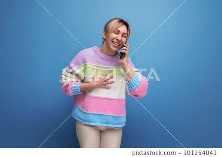 cheerful blond young woman in a striped jacket communicates by voice on a smartphone on a blue cheerful blond young woman in a striped jacket communicates by voice on a smartphone on a blue 101254041