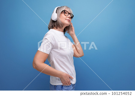 modern mature woman with gray hair listens to music in wireless headphones on studio background with 101254052