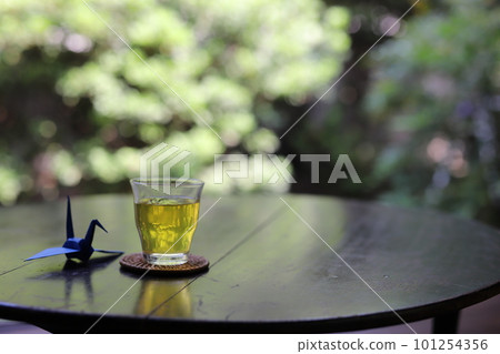 一杯茶和一隻摺紙鶴放在桌子上,在涼爽的門廊裡,背景是日本風景 一杯茶和一隻摺紙鶴放在桌子上,在涼爽的門廊裡,背景是日本風景 101254356