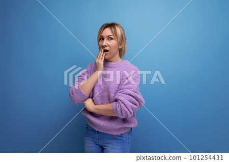 portrait of a cute pleasant blond young woman in a lavender sweater shocked on a bright plain 101254431