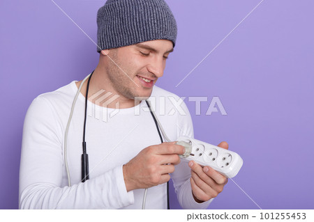 Portrait of young smiling electrician wearing gray cap and white shirt, radioman holding electric extender around his neck, looking at extension. Copy space foe advertisment or promotional text. Portrait of young smiling electrician wearing gray cap and white shirt, radioman holding electric extender around his neck, looking at extension. Copy space foe advertisment or promotional text. 101255453