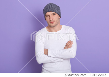 Studio shot of young man standing with hands folded wearing white casual shirt and gray cap. Copy space for advertisment or promotion text. Handsome mle looking directly at camera. People concept. 101255464