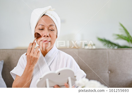 Beautiful Asian-aged woman doing makeup, applying brush on her cheek 101255693
