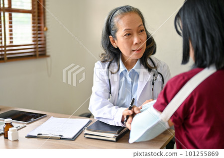 A professional senior Asian female orthopedic doctor consulting a surgery plan with a patient 101255869