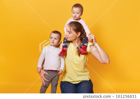 A happy mother holds one kid on her neck and another hug tight, having funny weekends together, looking after her children carefully. Spending weekends joyfully. Motherhood and care concept. A happy mother holds one kid on her neck and another hug tight, having funny weekends together, looking after her children carefully. Spending weekends joyfully. Motherhood and care concept. 101256831