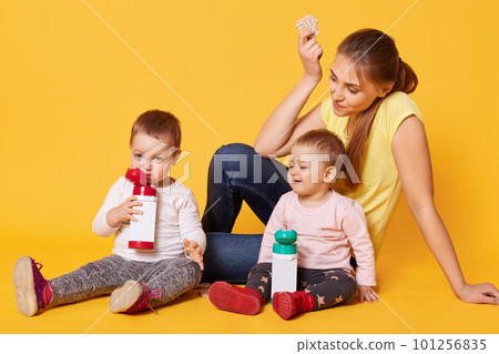 A positive loving mom cares her twin daughters, sits on the floor, being happy to spend time with little babies. Cheerful merry children are happy being withing the family circle. Chilcare concept. A positive loving mom cares her twin daughters, sits on the floor, being happy to spend time with little babies. Cheerful merry children are happy being withing the family circle. Chilcare concept. 101256835