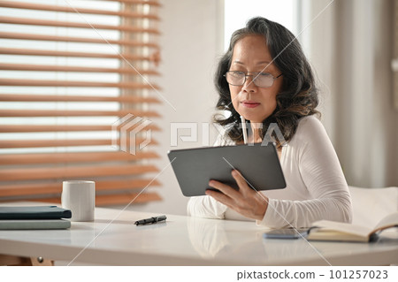 Senior Asian woman wearing glasses reading online news or shopping online on digital tablet  101257023