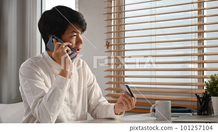 Handsome asian man with credit card and talking on mobile phone, connecting to mobile banking service 101257104