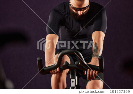 Portrait of a man on an exercise bike in the gym, a man with a beard and glasses on an exercise bike. Fitness man using exercise bike during cardio workout in crossfit gym. Portrait of a man on an exercise bike in the gym, a man with a beard and glasses on an exercise bike. Fitness man using exercise bike during cardio workout in crossfit gym. 101257399