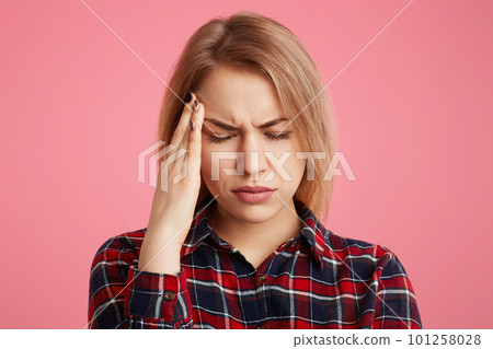 Close up portrait of stressful beautiful female student has headache after long exam preparation, closes eyes and scratches head, tries to overcome terrible pain, isolated over pink background Close up portrait of stressful beautiful female student has headache after long exam preparation, closes eyes and scratches head, tries to overcome terrible pain, isolated over pink background 101258028