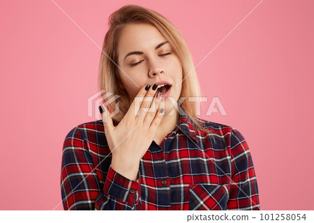 Tired light haired woman covers mouth with palm, closes eyes, dressed in checkered shirt, has manicure, wants to sleep, isolated over rosy background, has insomnia, feels fatigue working all night Tired light haired woman covers mouth with palm, closes eyes, dressed in checkered shirt, has manicure, wants to sleep, isolated over rosy background, has insomnia, feels fatigue working all night 101258054