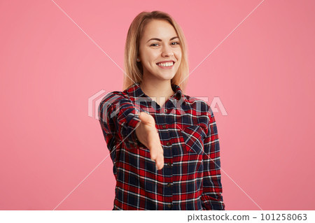 Beautiful blonde woman stretches hand in front, greets somebody, being glad to meet with friend, poses against pink background. Young female going to shake hands with somebody, gestures indoor Beautiful blonde woman stretches hand in front, greets somebody, being glad to meet with friend, poses against pink background. Young female going to shake hands with somebody, gestures indoor 101258063