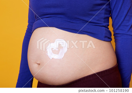 Faceless pregnant woman applying moisturizing cream on her belly, doing cosmetics procedures for preventing stretch marks isolated on yellow background. Pregnancy, maternity and expectation concept. 101258190