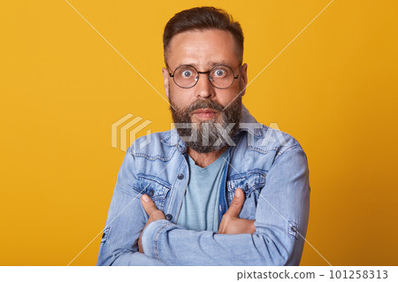 Portrait of shocked middle aged man in full disbelief. Hipster male with beard wears denim jacket posing isolated over yelow studio background. Astonished face expression, human emotion, body language Portrait of shocked middle aged man in full disbelief. Hipster male with beard wears denim jacket posing isolated over yelow studio background. Astonished face expression, human emotion, body language 101258313