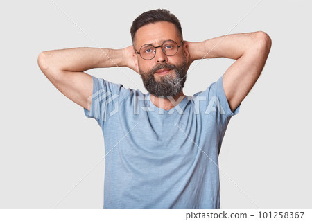 Confident relaxed calm man rises his arms, touching his head with both hands, having time for rest, looks quiet and peaceful. Slender charismatic man poses isolated over light gray background. Confident relaxed calm man rises his arms, touching his head with both hands, having time for rest, looks quiet and peaceful. Slender charismatic man poses isolated over light gray background. 101258367