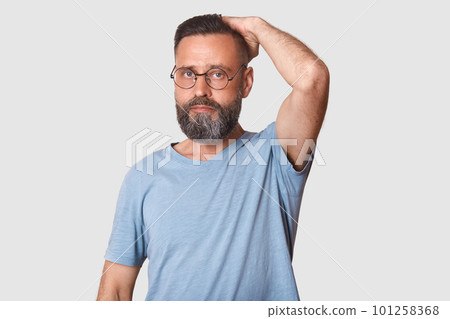 Middle aged good looking bearded man with fashionable spectacles wearing light blue casual t shirt, stands in front of camera, looking at it. hard working model poses isolated over light background. Middle aged good looking bearded man with fashionable spectacles wearing light blue casual t shirt, stands in front of camera, looking at it. hard working model poses isolated over light background. 101258368