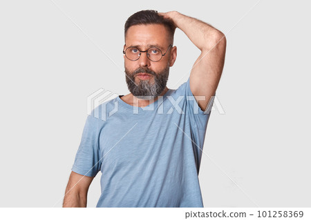Studio portrait of ordinary good looking middle aged man with beard wearing glasses and gray casual t shirtr, handsome male touching back of head,having serious facial expression. People concept. Studio portrait of ordinary good looking middle aged man with beard wearing glasses and gray casual t shirtr, handsome male touching back of head,having serious facial expression. People concept. 101258369