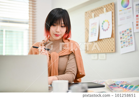 Charming Asian female graphic designer working on her new design project on laptop Charming Asian female graphic designer working on her new design project on laptop 101258651