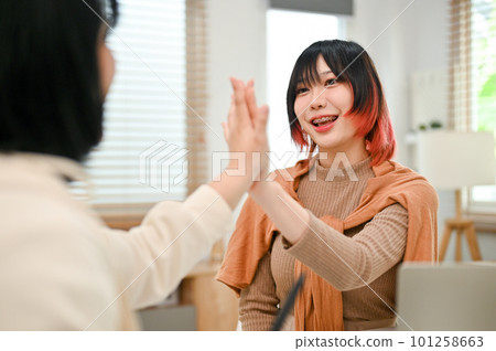 Cheerful Asian female worker giving high five to her colleague while working together 101258663