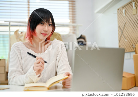 Attractive Asian female clothes shop owner taking online orders on her book. 101258696