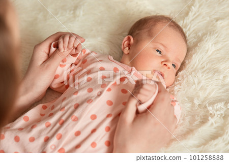 Close up portrait of newborn baby looking away, lying in bed on fluffy blanket, unknown person holding infants hands, faceless mother with her new born kid. Close up portrait of newborn baby looking away, lying in bed on fluffy blanket, unknown person holding infants hands, faceless mother with her new born kid. 101258888