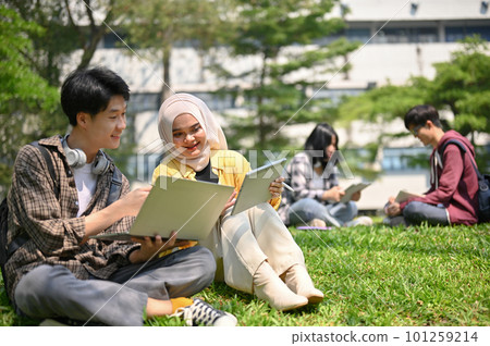 Two Asian college students are working on their schoolwork while sitting on the grass Two Asian college students are working on their schoolwork while sitting on the grass 101259214