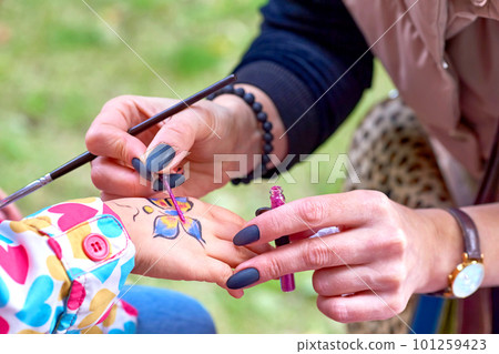 The artist draws a colorful butterfly on a child's hand 101259423