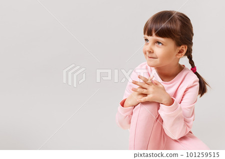 Beautiful cute little girl looks to the side with interest, dressed in pink clothes, has dark hair and two pigtails, copy space for advertisement, isolated over white background. 101259515