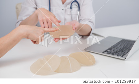 Caucasian woman and plastic surgeon touching and choosing breast implants.  101259917