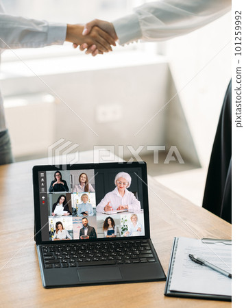 Online cooperation. Web chat. Digital conference. Female business partners working with team on laptop approving agreement deal with handshake at office interior with free space. 101259992