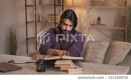 Book research. Home study. Knowledge education. Curious smart guy learning reading literature preparing for exam on couch at modern interior. 101260030