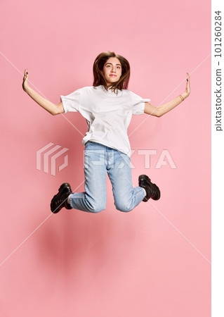 Full-length portrait of young, beautiful, brunette girl in casual clothes jumping against pink studio background. Relaxation 101260284