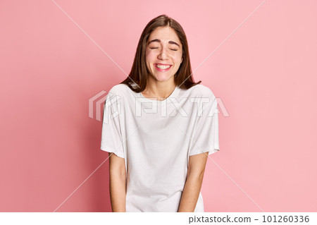 Happiness. Portrait of young positive, beautiful girl in white t-shirt posing, smiling against pink studio background. Celebration 101260336