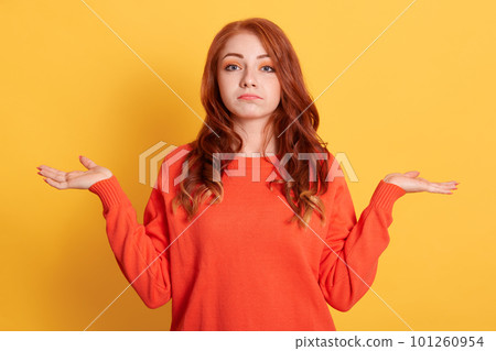 Confusion very offended red haired woman looking at camera with sad look and spreading her hands, wearing casual clothing, posing isolated over yellow wall. 101260954
