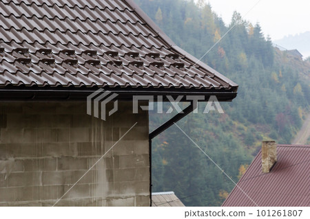 House with new brown metal tile roof and rain gutter. Metallic Guttering System, Guttering and Drainage Pipe Exterior House with new brown metal tile roof and rain gutter. Metallic Guttering System, Guttering and Drainage Pipe Exterior 101261807