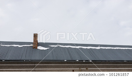 a brick chimney on a metal roof in the winter under the snow. construction concept a brick chimney on a metal roof in the winter under the snow. construction concept 101261857