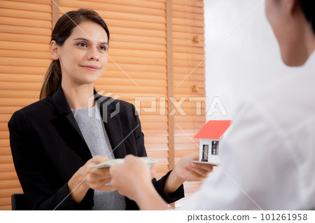 Young realtor woman giving house model to hands customer while client giving money. 101261958