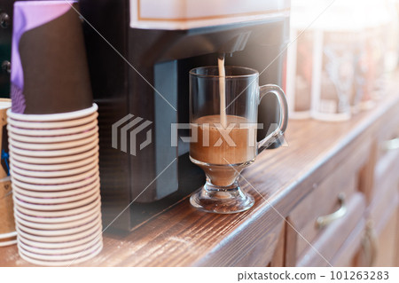 Coffee machine brewing cuppuccino coffee, stack of disposable paper cups, glass of tasty hot beverage on cafe's counter. Coffee machine brewing cuppuccino coffee, stack of disposable paper cups, glass of tasty hot beverage on cafe's counter. 101263283