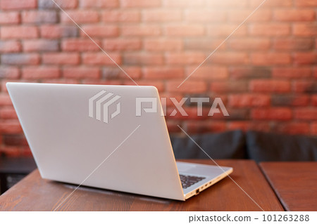 White laptop on wooden table against brick wall, online working in cafe shop, white note book on desk, workplace with laptop. 101263288