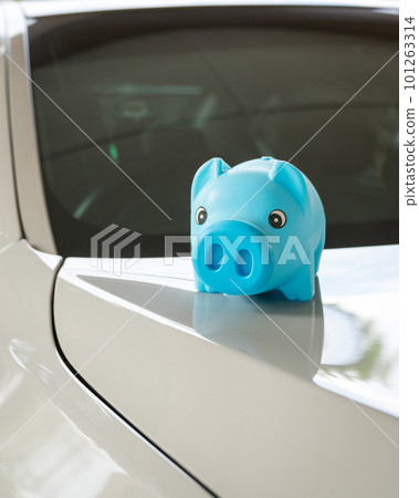 Blue piggy bank money box on top of white car bonnet. Blue piggy bank money box on top of white car bonnet. 101263314