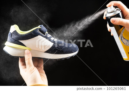 A woman applies a spray from a cylinder with a water-repellent liquid to children's shoe. Care for shoes, elimination of unpleasant odor. A woman applies a spray from a cylinder with a water-repellent liquid to children's shoe. Care for shoes, elimination of unpleasant odor. 101265061