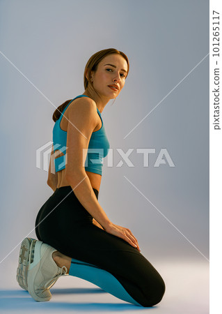 Sporty woman wearing sportswear is kneeling and posing on studio background. Healthy life concept 101265117