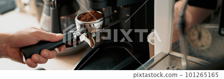 Close-up of male hand holding portfilter near coffee grinder 101265165